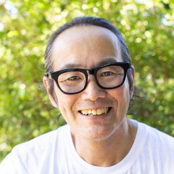 Portrait of Isekatsuya. A man with short hair and glasses. He is wearing a white shirt, smiling and facing forward.