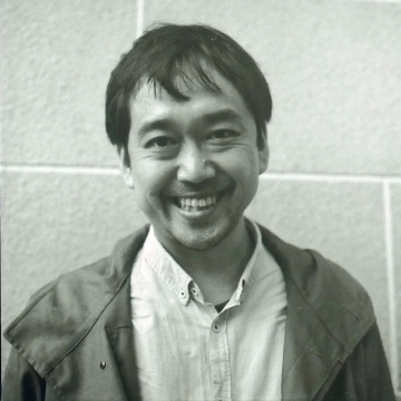 Portrait of Taru Matsui. A smiling man with a short cut. Black-and-white photograph. White shirt and black jacket.