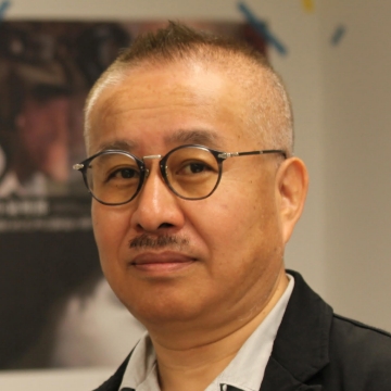 Portrait of Kazuji Mogi. A man with short hair and glasses. He wears a black jacket.