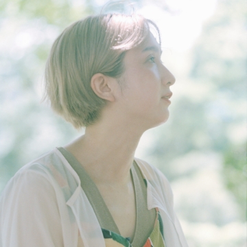 Portrait of Natsumi Wada. Woman facing sideways in a lot of light. The background is green.