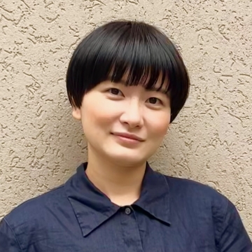 テイ・ウシンのポートレート ショートカットの女性。黒い襟付きシャツを着て微笑んでいる